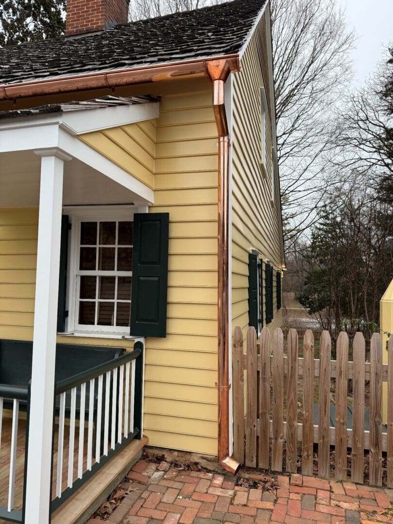 Yellow house with green shutters and fence.